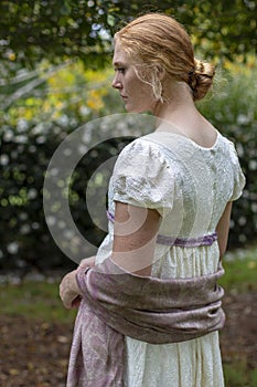 Regency woman in cream dress walks alone in a summer garden photo