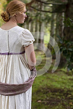 Regency woman in cream dress walks alone in a summer garden photo