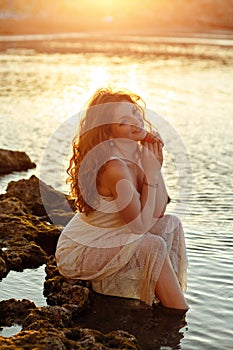 The red-haired sensual girl in white dress sitting on the rocks