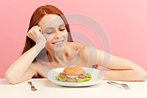 Red-haired skinny woman with greedy eyes being ready to eat burger.