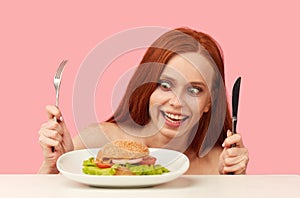 Red-haired skinny woman with greedy eyes being ready to eat burger.
