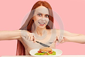 Red-haired skinny woman with greedy eyes being ready to eat burger.