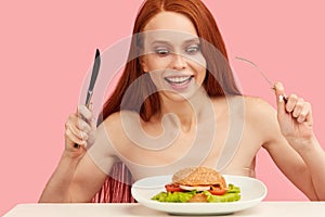 Red-haired skinny woman with greedy eyes being ready to eat burger.