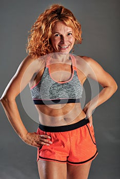 A red-haired and tanned sportswoman in orange shorts holds her hands on her hips.