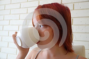 Red-haired teenage girl drinks tea from a white cup