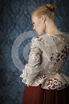 Red-haired 18th century woman standing in front of baroque wall paper