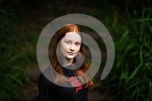 Red haired twelve year old girl with freckles posing with a nature bokeh background