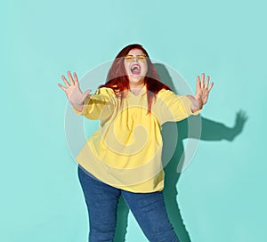 Red-haired voluptuous young woman screaming with closed eyes and showing stop by both hands.