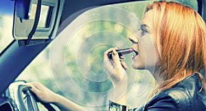 Red haired woman applying lipstick on lips in car. Danger on road.