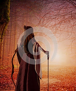 A red-haired woman archer of the Middle Ages with a bow in an autumn forest. Fantasy world
