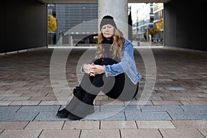 Red-haired woman with black jeans, black sweater and denim jacket in an urban location.