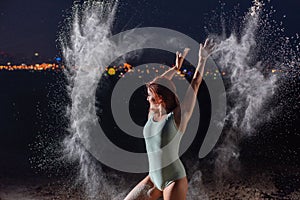 Red-haired woman in a blue bodysuit dancing in clouds of flour. A girl on the river bank jumping scattering white powder