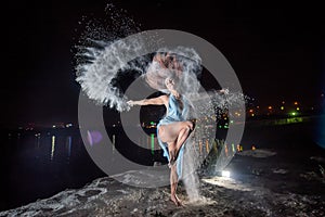 Red-haired woman in a blue dress with a deep neckline dancing in clouds of flour. A girl on the river bank jumping