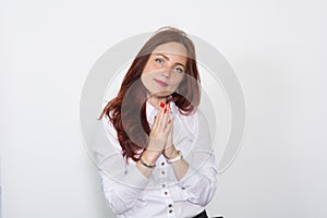 Red-haired woman in a bright blouse with hands clasped together on a white