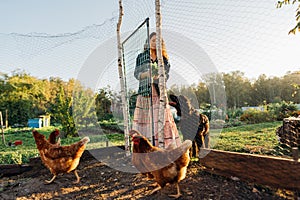 Red-haired woman farmer enters chicken coop to care and feed chickens at dawn