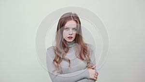 Red haired woman in gray sweater looks stylish and confident clasps her hands