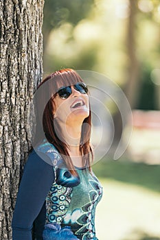 Red-haired woman laughing leaning against a tree. Selective focus.