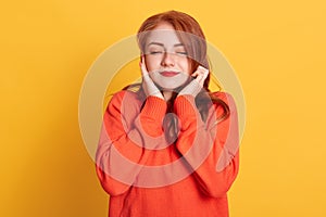 Red haired woman plugging ears with fingers and closing her eyes, not wanting to listen hard loud music, ignoring noise or