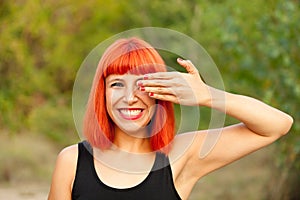 Red haired woman covering her eyes in a park