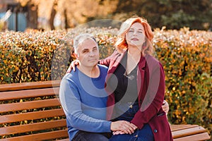 A red-haired woman sits on the lap of five-year-old man on a park bench in the fall