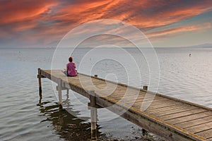 Red-haired woman sitting on a wooden dock watching the sunset