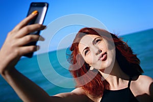 Red-haired woman takes selfie on smartphone camera.