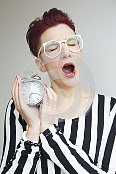 Red-haired woman yawning and holding alarm clock