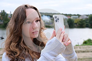 Red-haired young girl taking selfie with her smartphone against snowy background. Selective focus