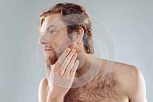 Red haired young man is stroking beard.