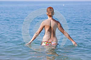 Red haired young woman in swimming trunks entering in sea