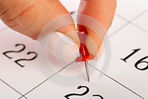 Beautiful female Hand with manicure pushes a red pin on a calendar 22 day