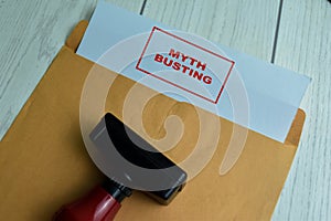 Red Handle Rubber Stamper and Myth Busting text above brown envelope isolated on wooden background