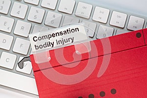 Red hanging folder on a keyboard has a tab with the words Compensation bodily injury on it
