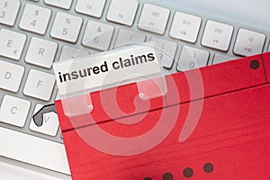 Red hanging folder on a keyboard has a tab with the words insured claims on it photo
