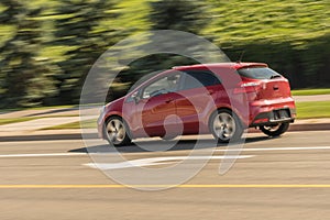 Red hatchback small car speeding near the green hill