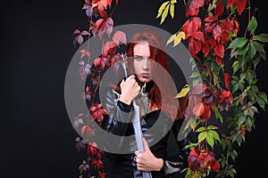 Red head girl among leaves holding a sword