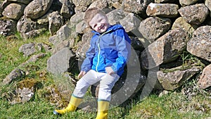 Red headed boy with blue jacket and yellow boots having fun playing on lane on a farm