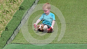 Red headed boy with a blue t-shirt having fun having fun on a grass slide in tha Playpark on a sunny day