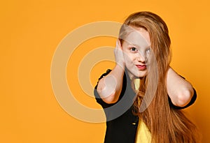 Red-headed teenage kid in black jacket and yellow t-shirt. She closed her ears with hands, posing on orange background. Close up