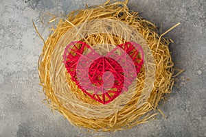 Red heart in a bird`s nest. The theme of love, family and the day of the holy valentine. View from above.