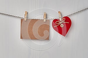 Red heart and blank card hanging on the clothesline on white wooden background