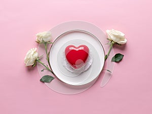 Red heart cake on white plate and delicate white roses.