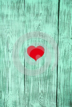 The red heart is carved in a wooden board of green color. Background.