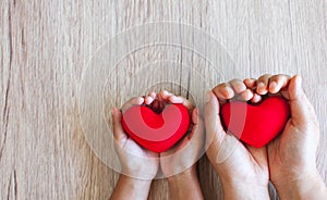 Red heart in child hands and parent hands on wooden table background