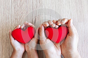 Red heart in child hands and parent hands on wooden table background