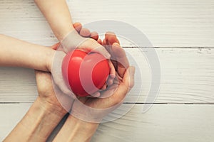 Red heart in child and mother hands on white wooden background. concept of love, charity, empathy