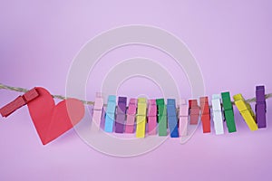 Red heart and colorful paper clips on rope on soft pink purple background.