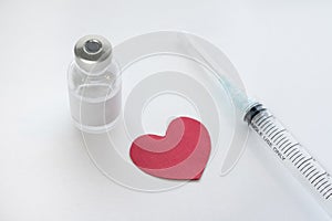 Red heart displayed with a medical vial of injectible medicine and hypodermic needle