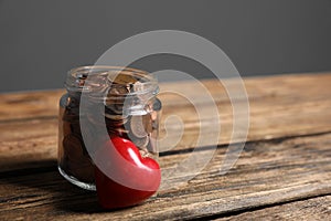 Red heart and donation jar with coins on table against grey background. Space for text