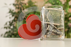 Red heart and donation jar with money on table